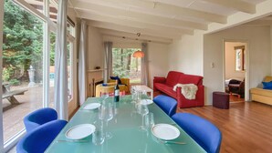 Een eetgedeelte met een glazen tafel, gedekt voor zes personen, omringd door blauwe stoelen. Op de achtergrond is een rode bank en een gele fauteuil te zien.