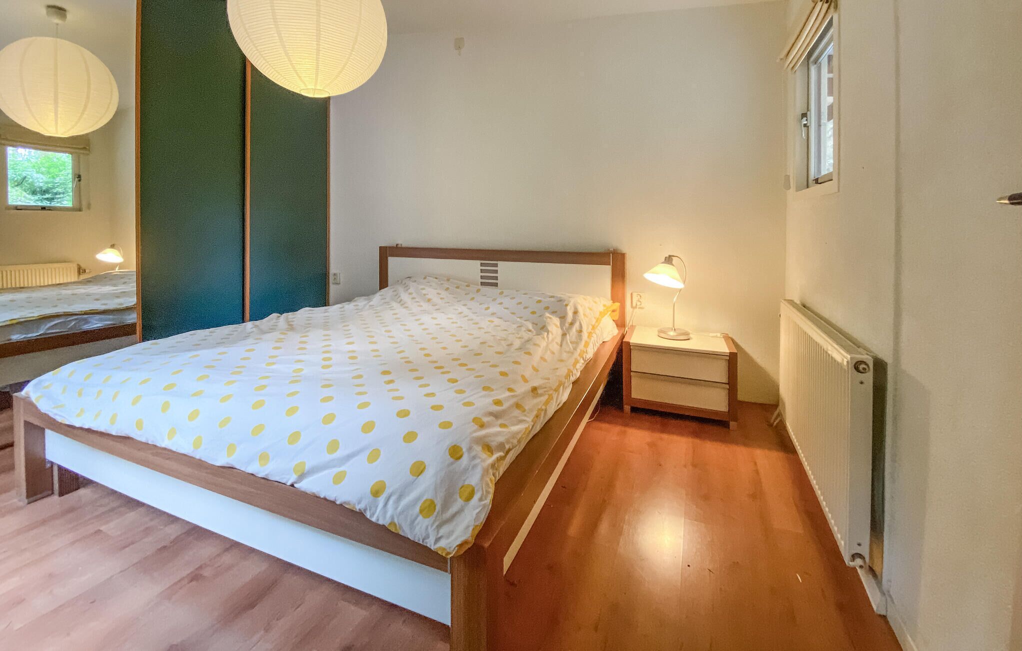 Ein Schlafzimmer mit einem Bett, Nachttischen, einer Lampe, einer Heizung und einem Fenster.