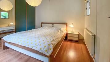 Ein Schlafzimmer mit einem Bett, Nachttischen, einer Lampe, einer Heizung und einem Fenster.