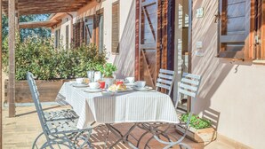 Une table dressée à l’extérieur, recouverte d’une nappe à rayures, entourée de chaises en métal, et surmontée d’une tonnelle en bois.