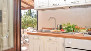 Une cuisine avec des meubles blancs, un plan de travail en bois, un évier et une fenêtre donnant sur un jardin.