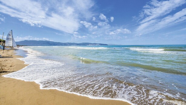 Une plage avec un ciel dégagé, des vagues douces et une chaîne de montagnes à l’horizon.