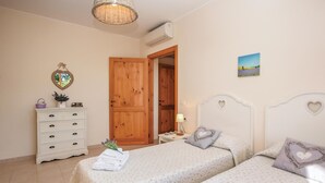 Une chambre avec deux lits, une commode, une porte et une petite table avec une lampe.