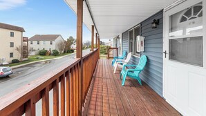 Une terrasse en bois avec un porche couvert, une porte blanche avec moustiquaire et deux chaises turquoise.
