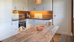 A kitchen with white cabinets, a wooden table, and a hanging light fixture.