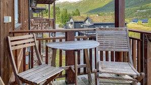 A wooden deck with two chairs and a table, overlooking a mountainous landscape.