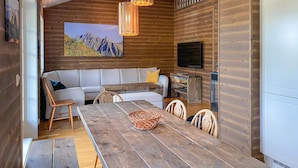 A cozy cabin interior with a wooden dining table, a sofa, and a television.