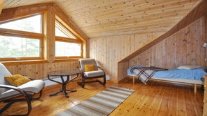 A cozy cabin room with wooden walls, a bed, a chair, a table, and large windows. - Beautiful home in Koppom with sauna (Koppom)