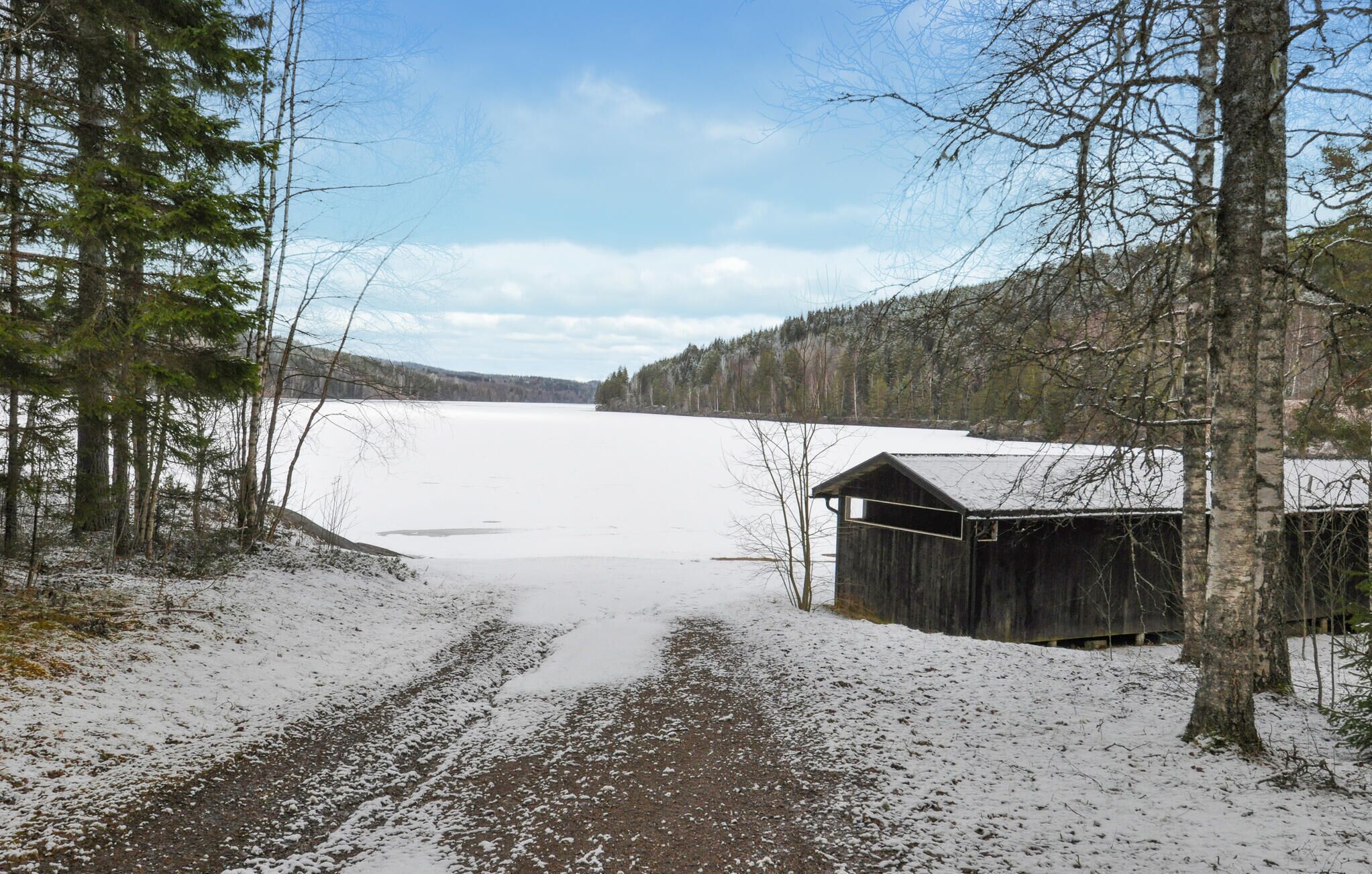 Paisatge cobert de neu amb una cabana de fusta i un llac gelat.