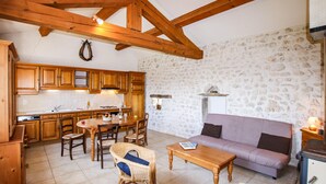 Una cocina rústica con armarios de madera y una pared de piedra. Hay una mesa de comedor con sillas y un sofá en la sala de estar.