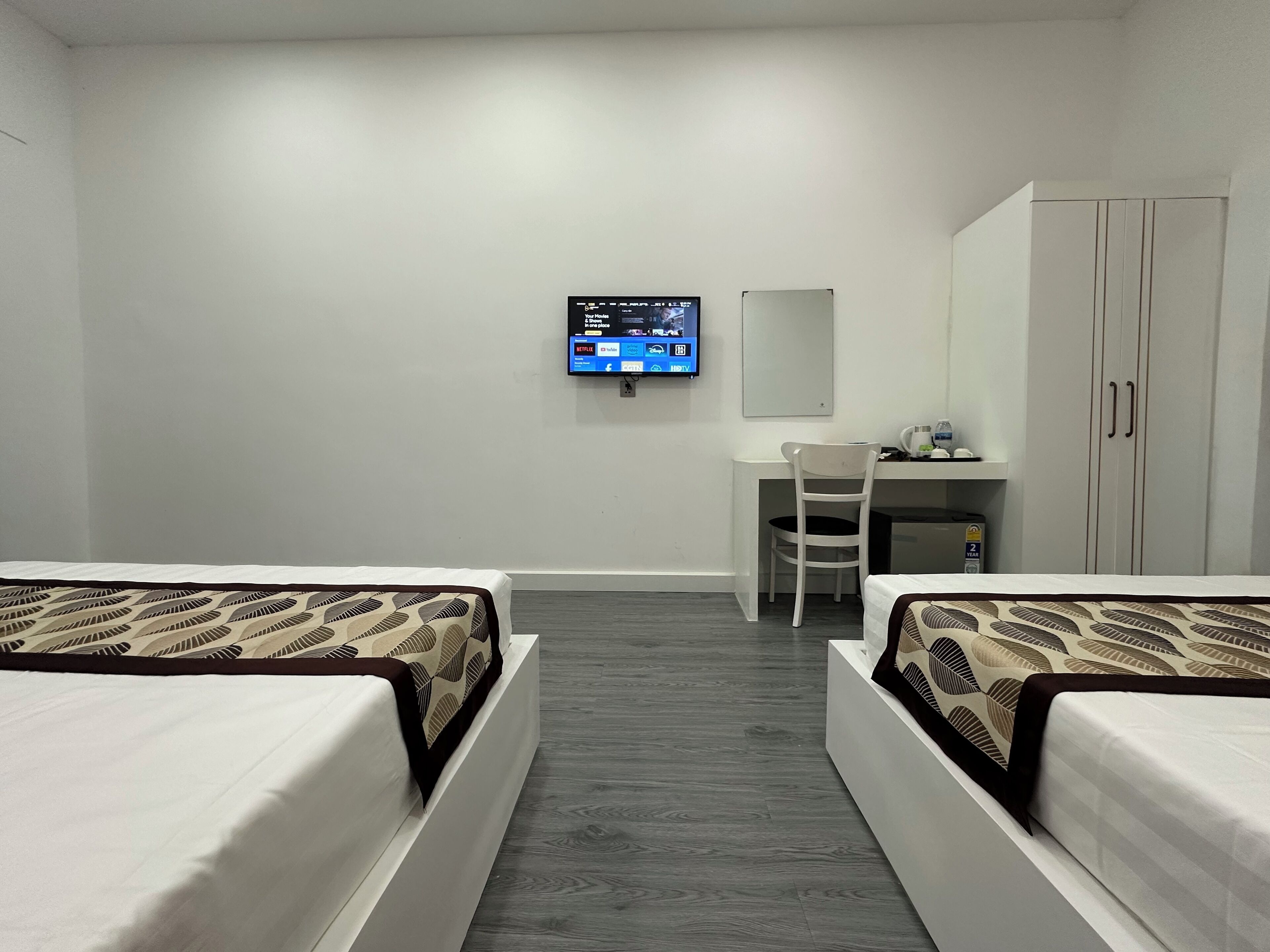 Une chambre d’hôtel avec deux lits, un bureau, une chaise, un téléviseur fixé au mur et une armoire.