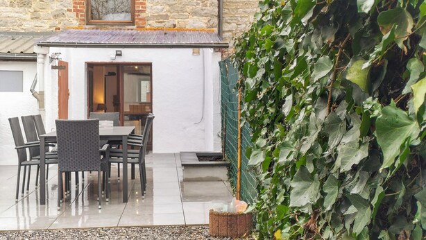 An outdoor patio with a table and chairs, a stone wall, and a large green ivy-covered wall. - 2 bedroom pet friendly home in Treignes (Treignes)