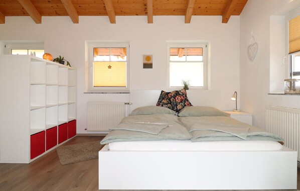 A bedroom with a bed, a white wardrobe with red doors, two windows with blinds, and a radiator.