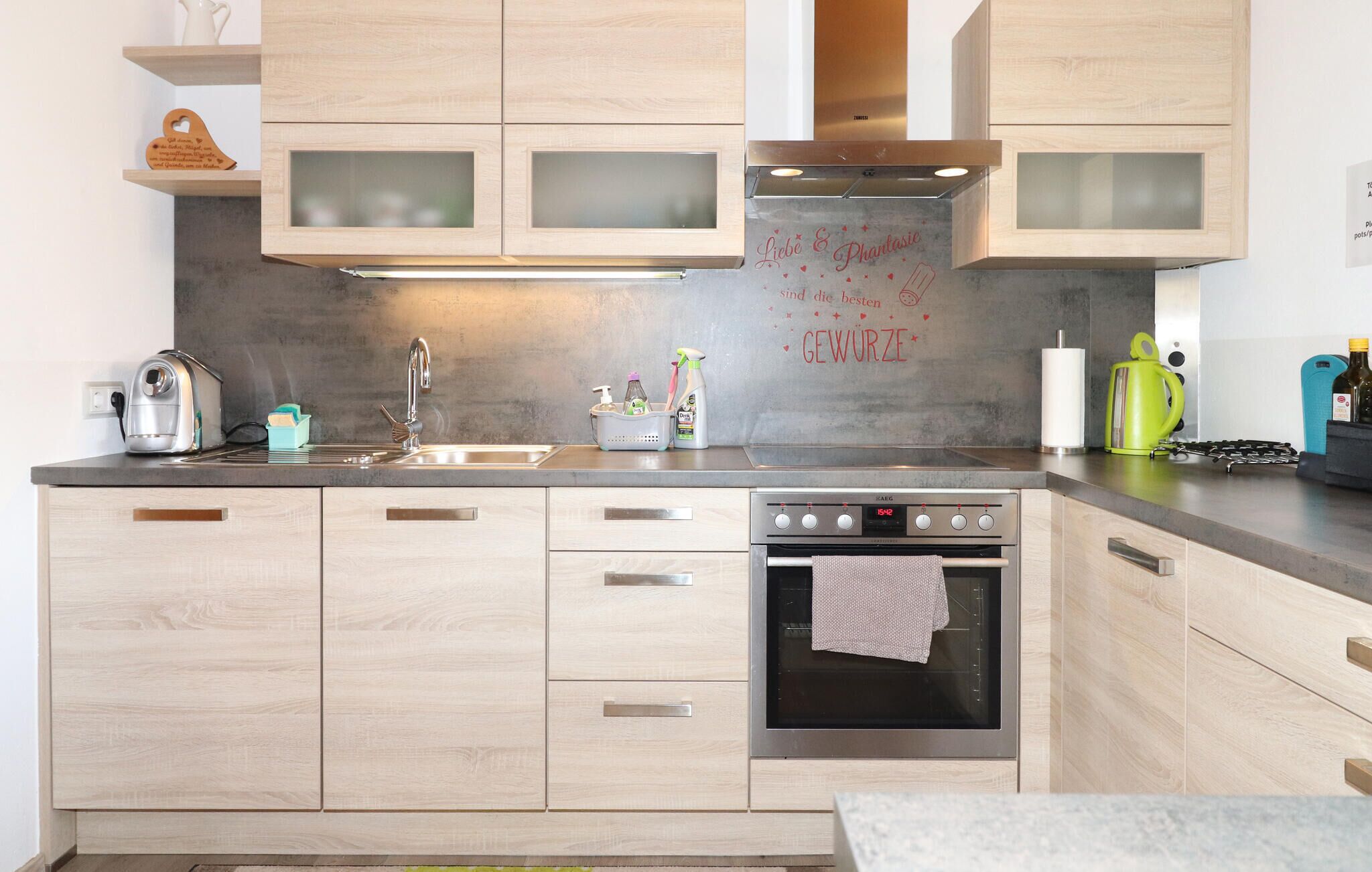 A modern kitchen with light wood cabinets, a stainless steel range, and a built-in oven.