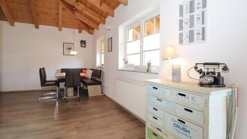 Een gezellige kamer met een houten plafond, een zithoek met een bank en stoelen, een radiator en een vintage telefoon op een dressoir.