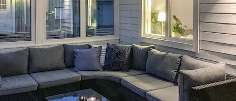 A cozy living room with a sectional sofa, a coffee table with candles, and large windows with exterior views.