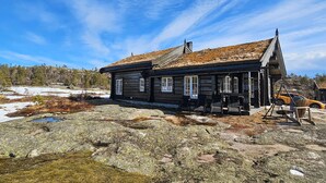 Une cabane en rondins avec un toit à forte pente, de nombreuses fenêtres et une véranda avec des chaises.