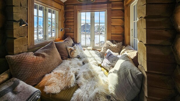 L’intérieur chaleureux d’un chalet en bois, avec un canapé moelleux, des couvertures douillettes et une grande fenêtre donnant sur un paysage enneigé.