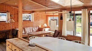 A wooden cabin interior with a dining area, sofa, and a view of the outdoors.