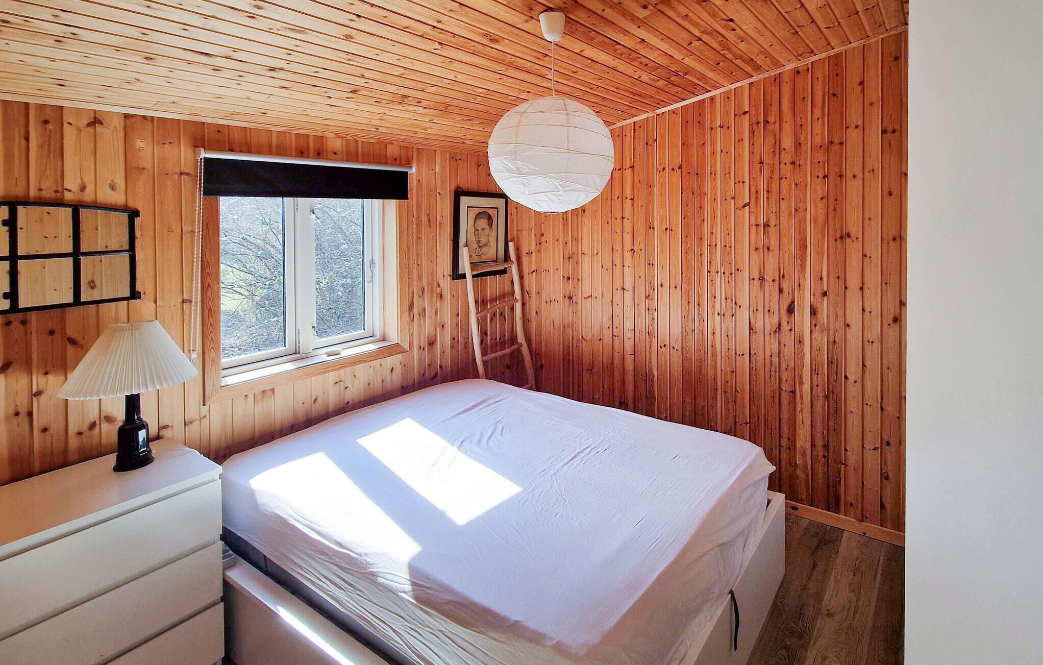 Camera da letto con pannelli in legno, un letto, una finestra, una lampada e un quadro appeso al muro.