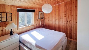 A wooden-paneled bedroom with a bed, a window, a lamp, and a picture on the wall.