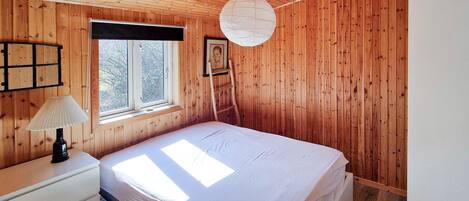 Camera da letto con pannelli in legno, un letto, una finestra, una lampada e un quadro appeso al muro.