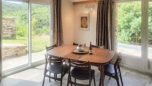 A dining area with a round table, four chairs, a wine bottle, and a decorative glass on a woven mat. - 3 bedroom stunning home in Vieussan (Vieussan)
