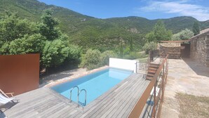 A swimming pool with a wooden deck, surrounded by stone walls and lush greenery. - 3 bedroom stunning home in Vieussan (Vieussan)