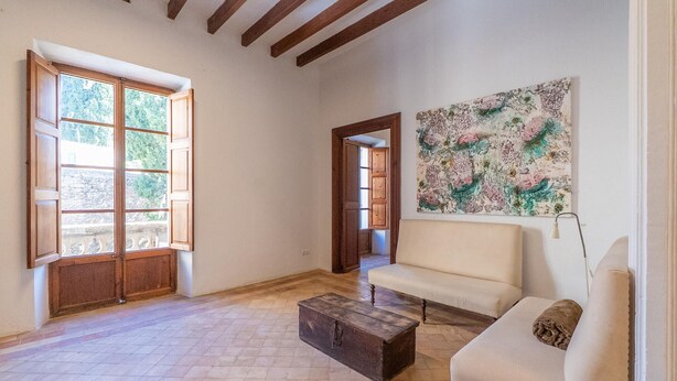 A spacious room with a large window, a sofa, a wooden chest, and a painting on the wall.