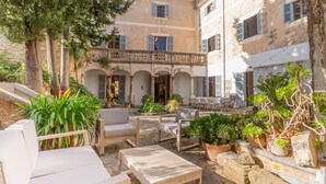 A courtyard with outdoor seating, including chairs and a table, surrounded by potted plants and trees.