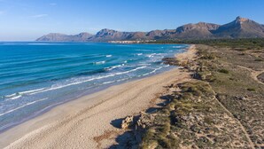 A coastal landscape with a sandy beach, clear blue sea, and distant mountains.