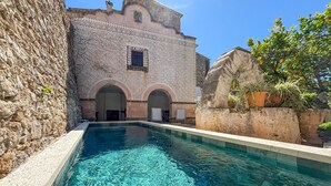 A pool area with clear water, stone walls, and a building with arches and a tiled facade.