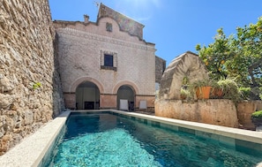 A pool area with clear water, stone walls, and a building with arches and a tiled facade. - Awesome home in Artà with WiFi (Artà)