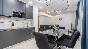Cozinha moderna com armários escuros, bancada de mármore e área de jantar com mesa de vidro e cadeiras pretas.
