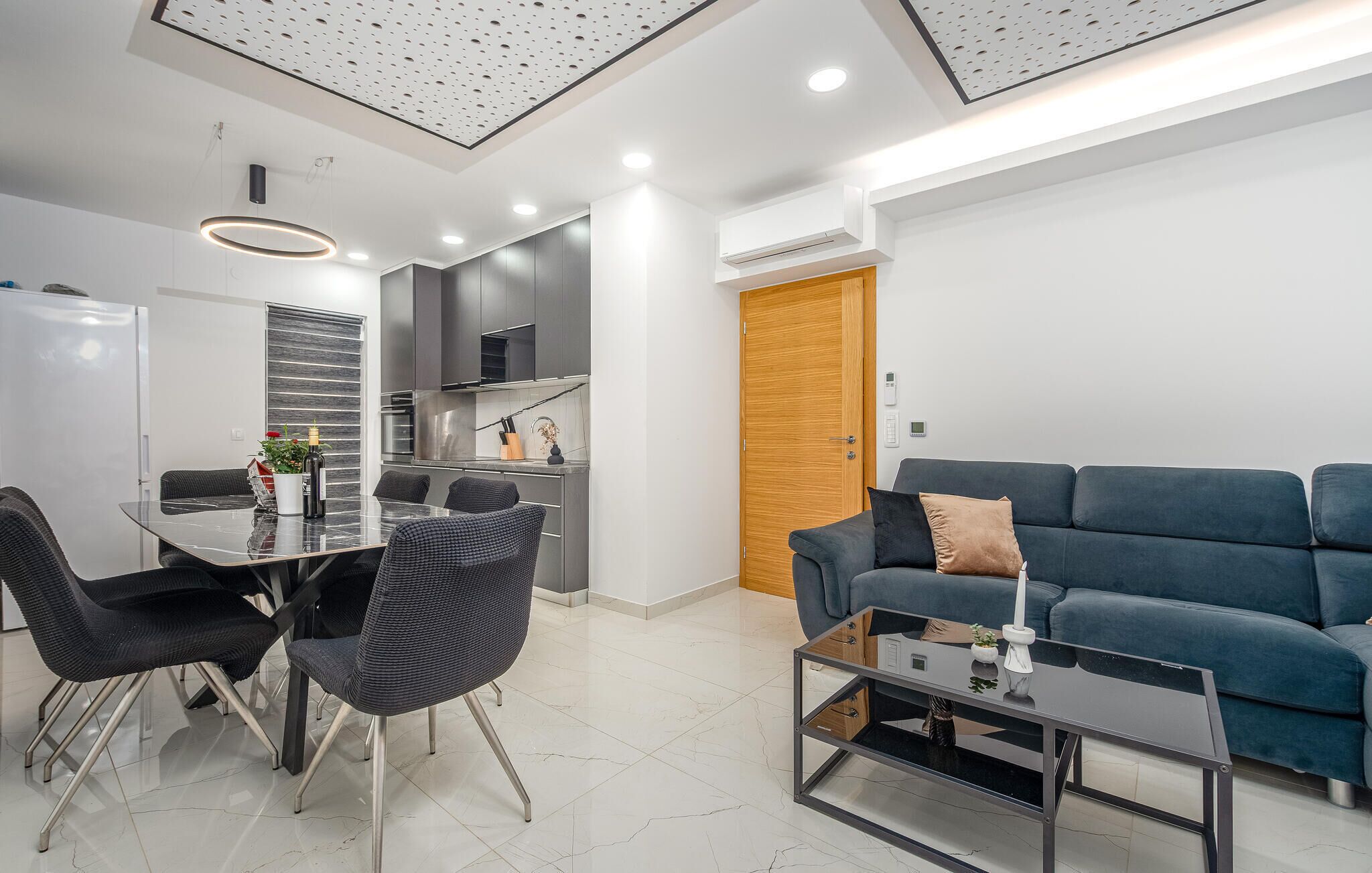 A modern living room with a blue sofa, a glass coffee table, and a dining area with a glass table and chairs.