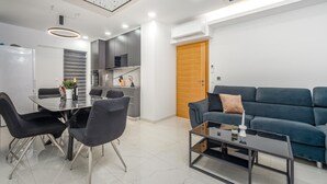 Uma sala de estar moderna com um sofá azul, uma mesa de centro de vidro e uma área de jantar com uma mesa e cadeiras de vidro.