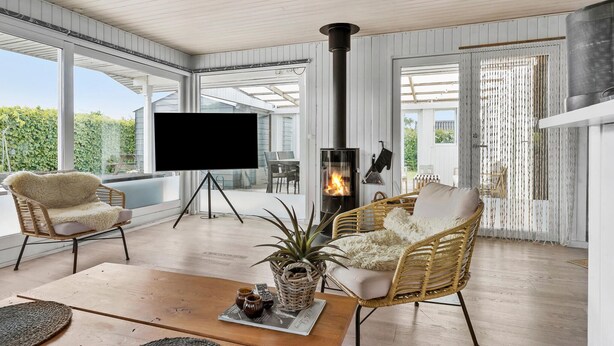 A modern living room with a fireplace, wicker furniture, and a large window overlooking a garden.