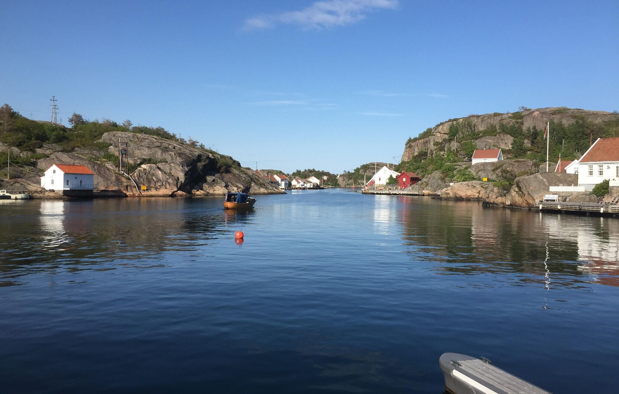 Un port tranquille avec un petit bateau, des maisons sur des collines rocheuses et un ciel dégagé.