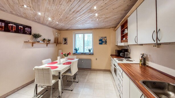 Una cocina con techo de madera, armarios blancos, una mesa de comedor con sillas y una ventana con persianas.