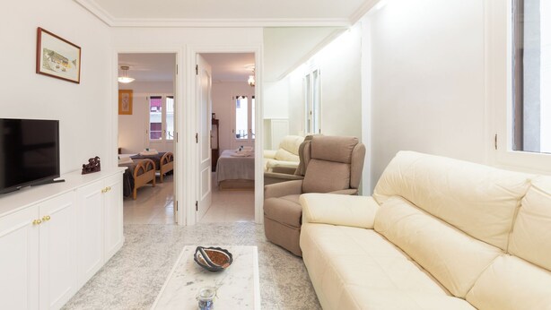 Una sala moderna con una televisión de pantalla plana, un sofá color beige, una mesa de centro y una zona de comedor con una mesa y sillas.
