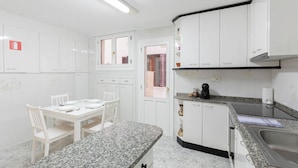 Cocina compacta con armarios blancos, encimera de granito y comedor con cuatro sillas blancas y una mesa dispuesta para cuatro.