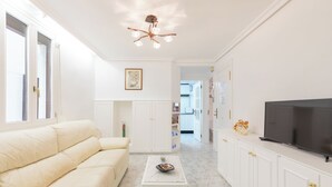 Una sala de estar moderna con un sofá color crema, una pequeña mesa de centro blanca y un televisor sobre un mueble.
