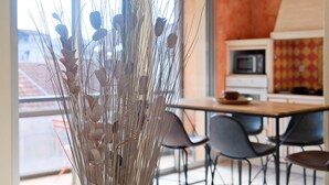 Ein Essbereich mit Tisch und Stühlen, eine Vase mit Trockenpflanzen und eine Küche im Hintergrund.