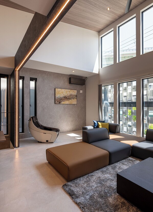 A spacious living area with a modern sofa set, a massage chair, and large windows offering a view of the city. - Universal front villa Sanrriott (Osaka)