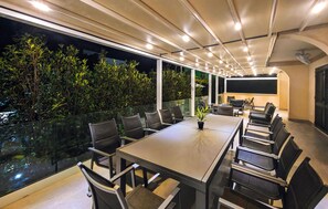 A modern outdoor dining area with a long table and chairs, surrounded by glass railings and a view of greenery. - Luxurious home in Kastel Stafilic (Kastel Stafilic)