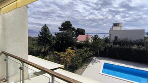 A balcony with a glass railing overlooking a swimming pool, a red-roofed house, and a mountainous landscape. - Luxurious home in Kastel Stafilic (Kastel Stafilic)