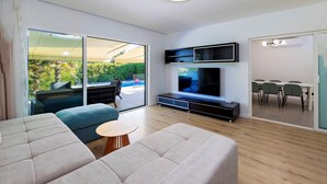 A modern living room with a large TV, a sofa, a coffee table, and a dining area visible through a glass door. - Luxurious home in Kastel Stafilic (Kastel Stafilic)