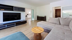 A modern living room with a large flat-screen TV, a grey sofa, a wooden coffee table, and a blue armchair. - Luxurious home in Kastel Stafilic (Kastel Stafilic)