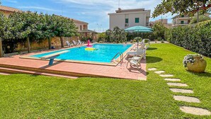 Ein rechteckiger Pool mit Fliesen umgeben von einem gepflegten Rasen und einem Kiesweg.