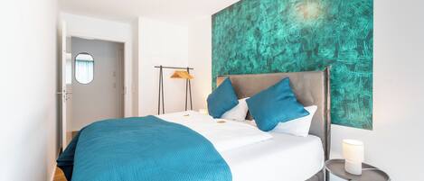 Un dormitorio moderno con una cama grande, ropa de cama color turquesa, un cabecero gris y una obra de arte abstracta color turquesa en la pared.